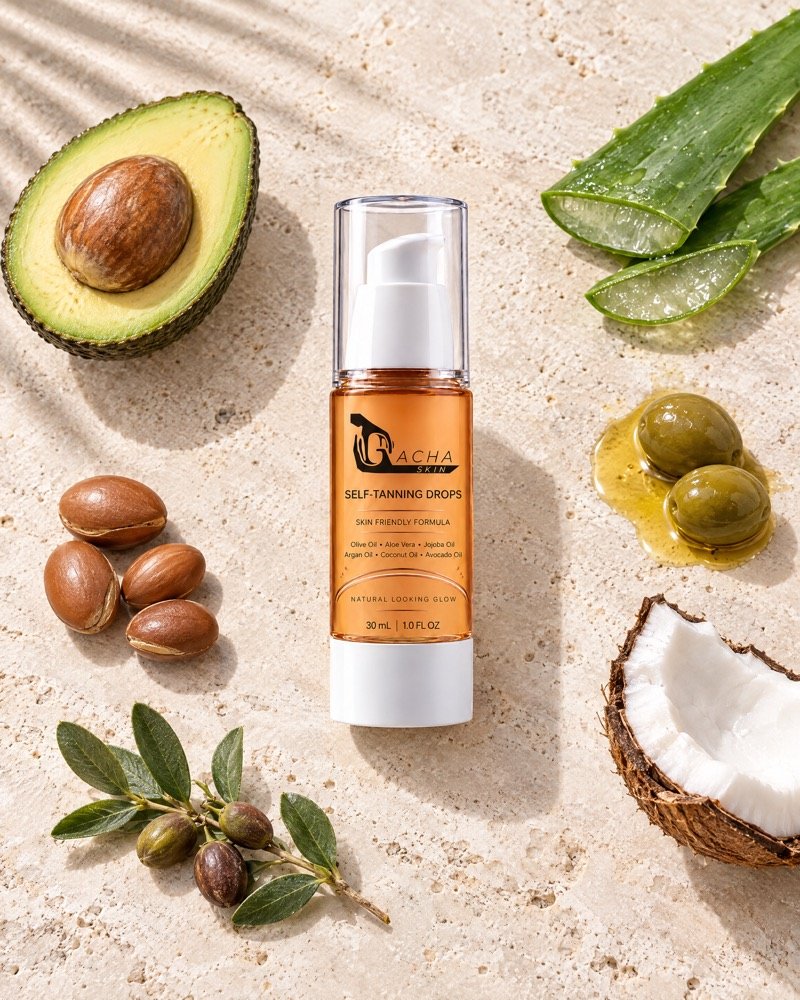The Gacha Self-Tanning Drops bottle on pale travertine, surrounded by half an avocado, split aloe vera, olives in olive oil, cracked coconut, argan nuts and a jojoba sprig.