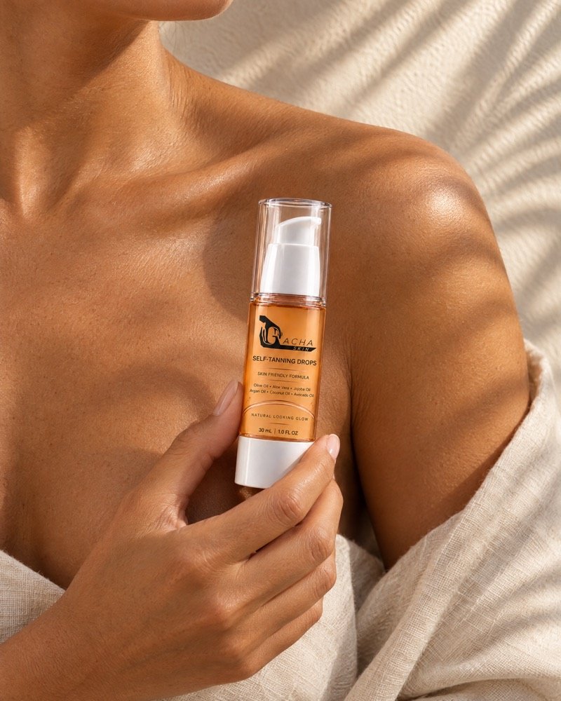 Close crop of a shoulder and collarbone with a natural-looking golden tan in late-afternoon light, a hand holding the Gacha Self-Tanning Drops bottle.